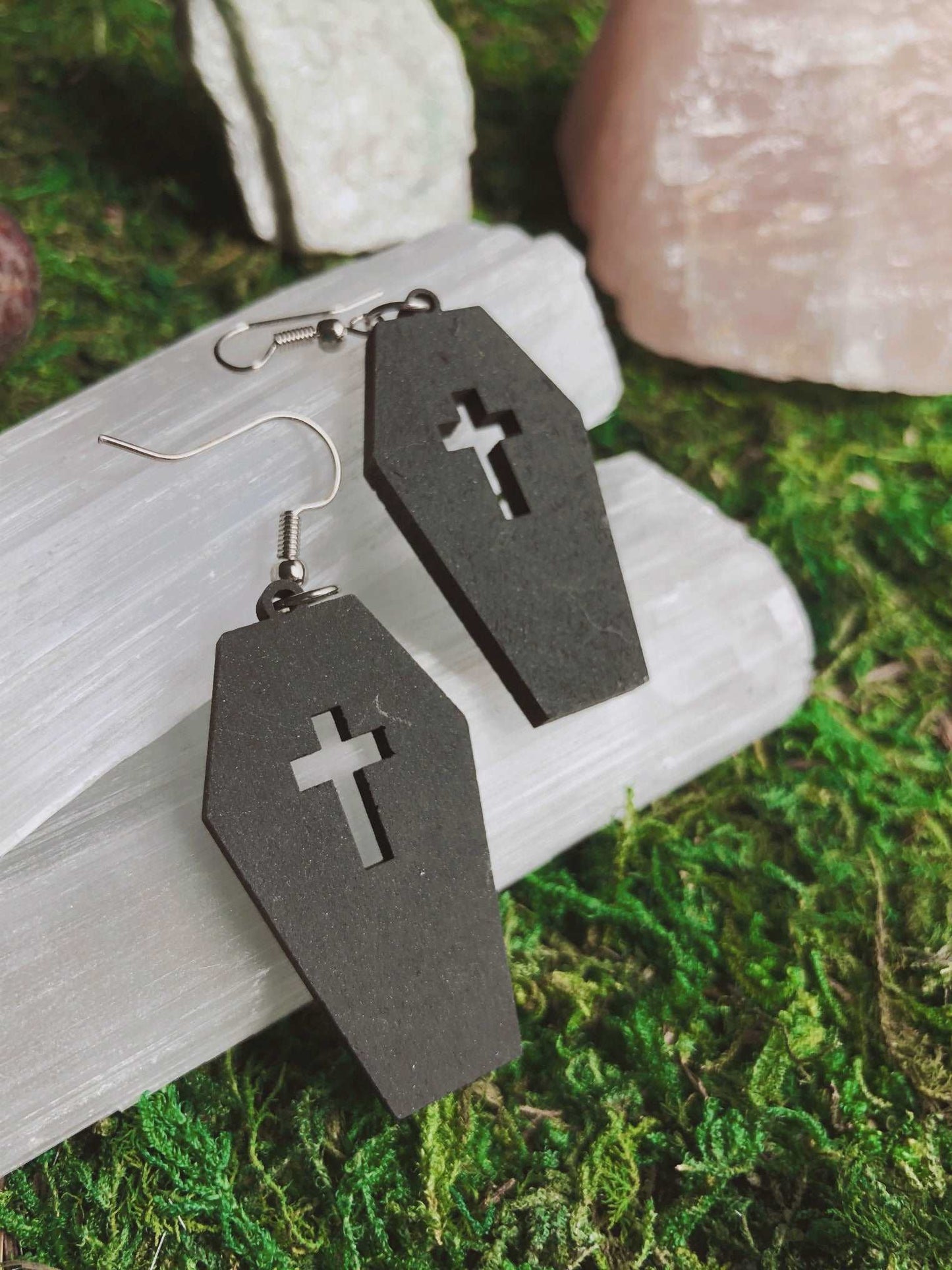 Pictured is a pair of earrings featuring a black coffin with a cut out cross on top. They are made of wood. Black Coffin Earrings