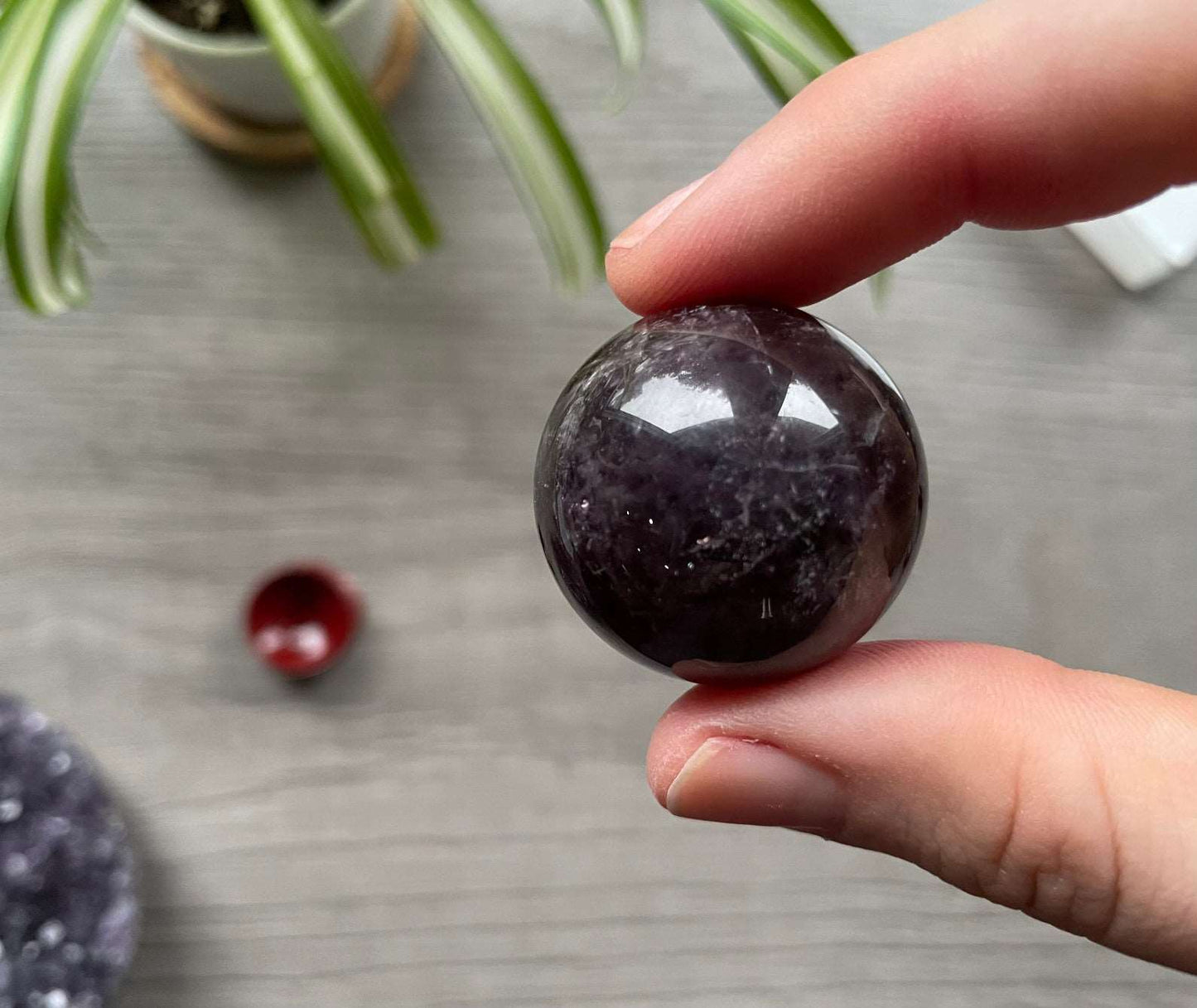 A polished sphere of amethyst is shown in the image. The crystal is a purple color and has a smooth, shiny surface. Amethyst Crystal Sphere 30mm (A)