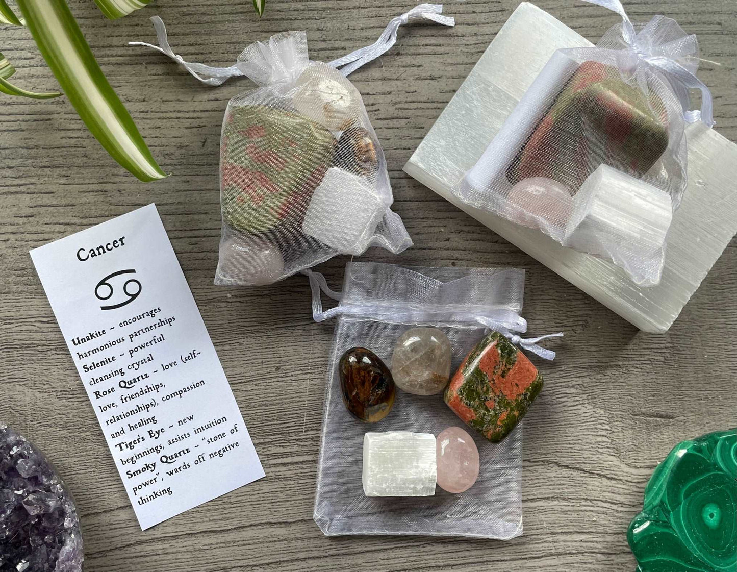 An image of a collection of tumbled stones in an organza bag. To the side is a piece of paper that describes what each tumbled stone's metaphysical properties are. CANCER Zodiac Tumbled Crystal Bag