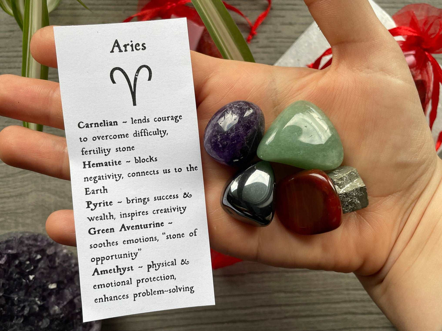 An image of a collection of tumbled stones in an organza bag. To the side is a piece of paper that describes what each tumbled stone's metaphysical properties are. ARIES Zodiac Tumbled Crystal Bag crystals