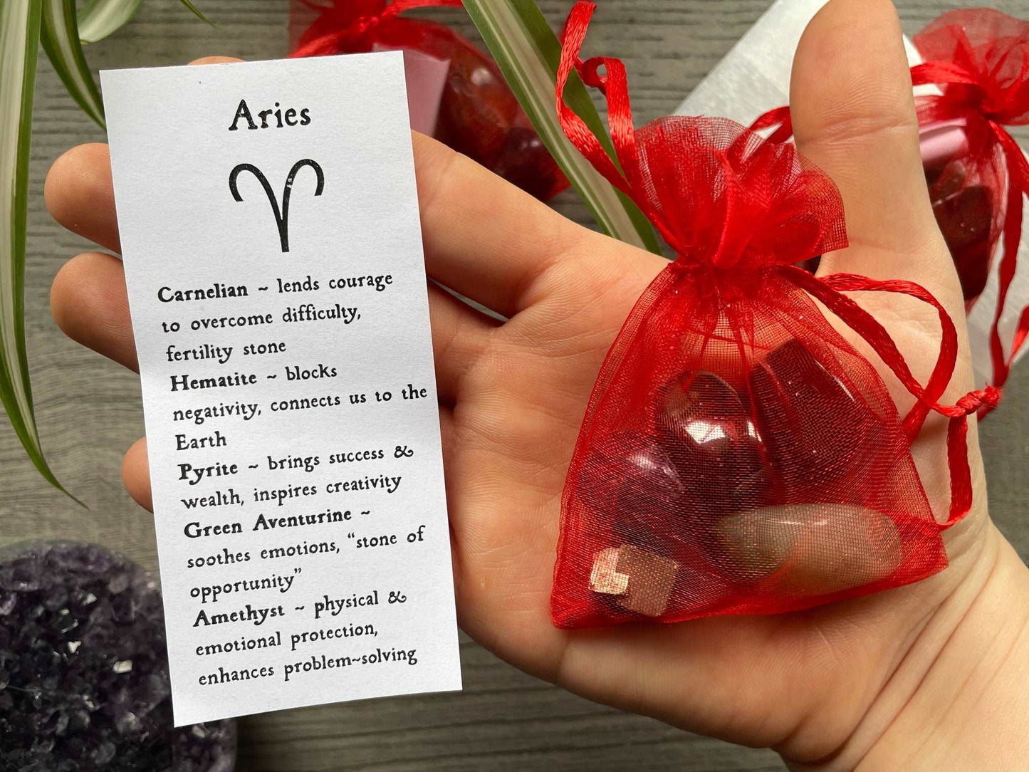 An image of a collection of tumbled stones in an organza bag. To the side is a piece of paper that describes what each tumbled stone's metaphysical properties are. ARIES Zodiac Tumbled Crystal Bag close up