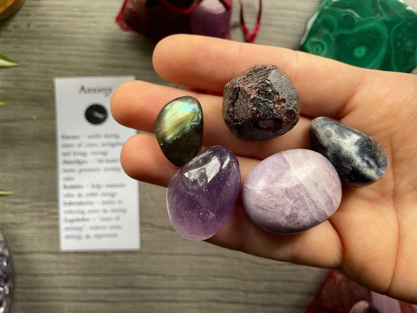 An image of a collection of tumbled stones in an organza bag. To the side is a piece of paper that describes what each tumbled stone's metaphysical properties are. ANXIETY Tumbled Crystal Bag close up