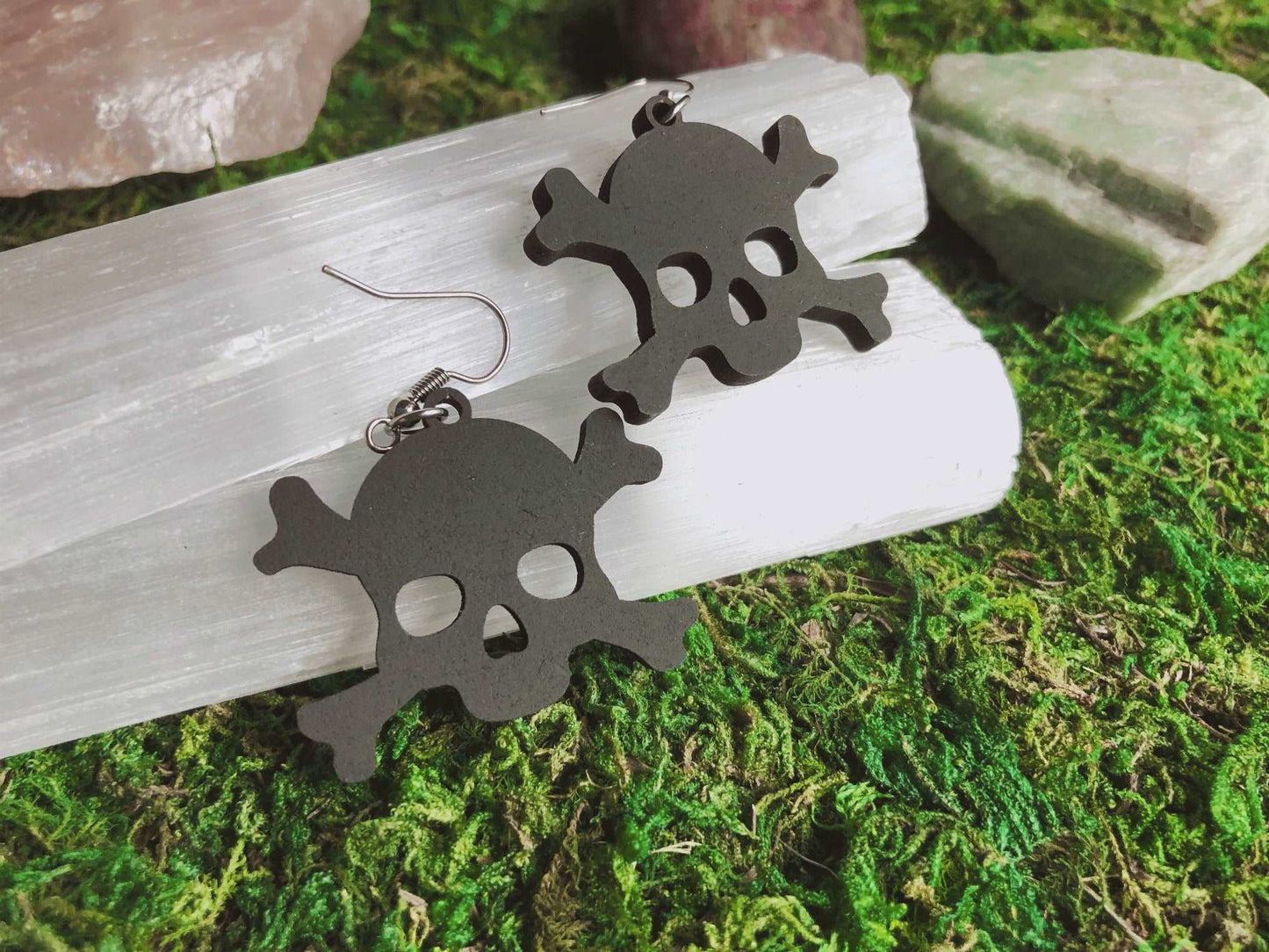 Pictured is a pair of earrings featuring a black skull and crossbone. They are made of wood. Black Skull and Crossbone Earrings