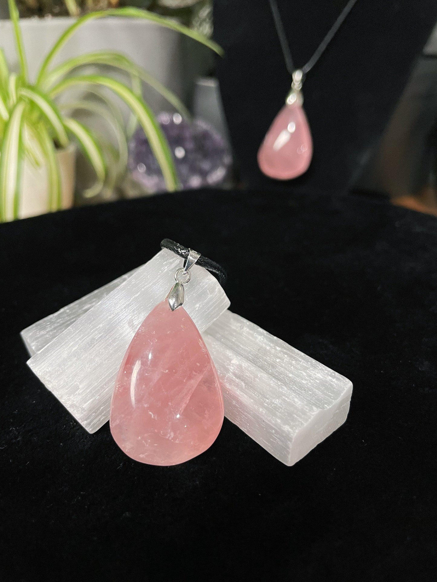 An image of a pink rose quartz teardrop shaped pendant on a necklace. It sits atop some selenite chunks and a black velvet surface. Rose Quartz Hand-Carved Teardrop Pendant Necklace crystal