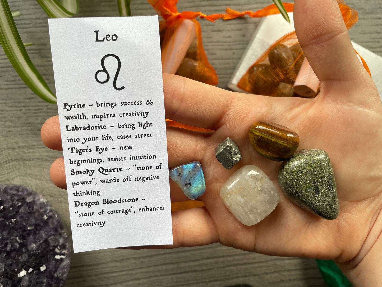 An image of a collection of tumbled stones in an organza bag. To the side is a piece of paper that describes what each tumbled stone's metaphysical properties are. LEO Zodiac Tumbled Crystal Bag crystals