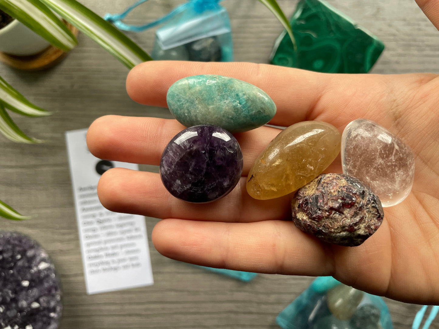 An image of a collection of tumbled stones in an organza bag. To the side is a piece of paper that describes what each tumbled stone's metaphysical properties are. SPIRITUAL STRENGTH Tumbled Crystal Bag close up