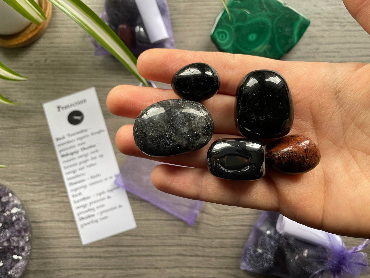 An image of a collection of tumbled stones in an organza bag. To the side is a piece of paper that describes what each tumbled stone's metaphysical properties are. PROTECTION Tumbled Crystal Bag close up