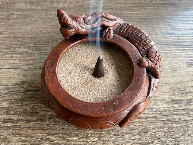 Pictured is a brown incense sand holder in the shape of a bowl with a dragon laying on the side of the bowl. Dragon Ceramic Incense Bowl with Sand