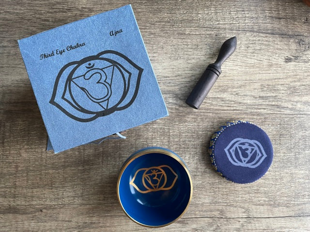 Pictured is a small metal singing bowl with a pillow and a wood gong mallet. Indigo Singing Bowl (Third Eye Chakra) top