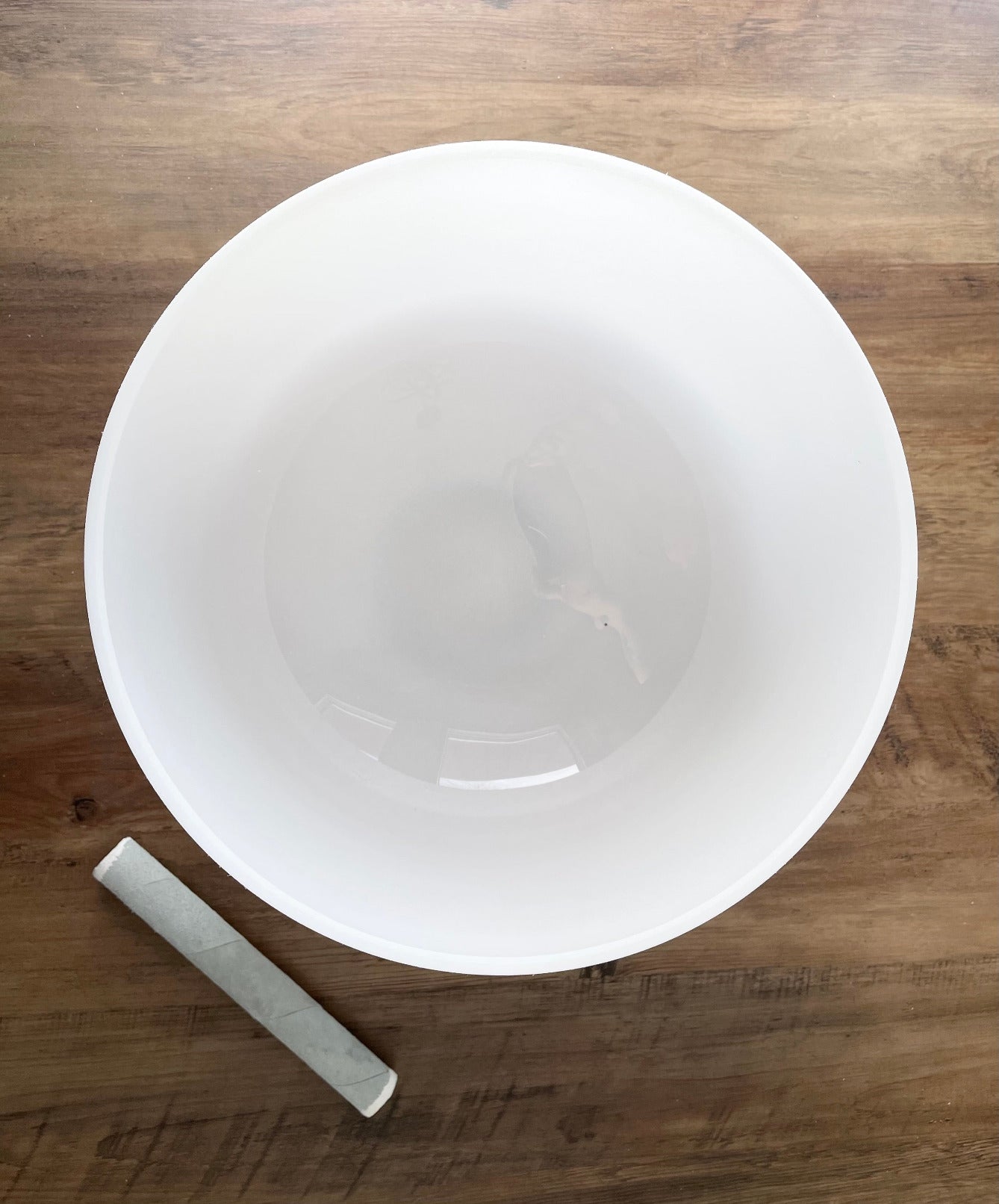 A photo of a quartz crystal singing bowl and a mallet on a wooden surface. The crystal singing bowl is made of clear quartz and has a smooth, round shape. 13" Crystal Singing Bowl (Frosted White) C4 top