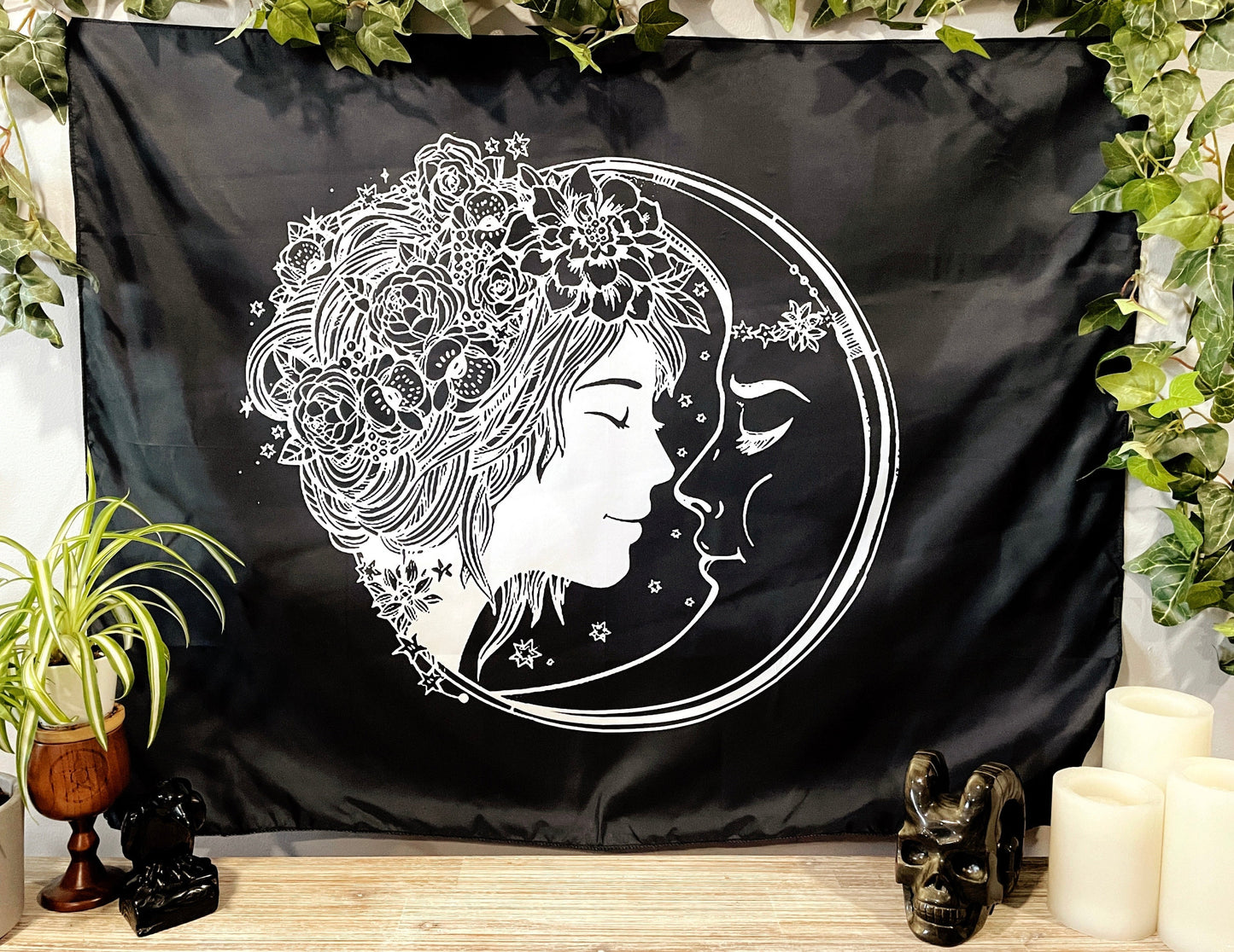 Pictured is a large wall tapestry with a black background and a woman with flowers in her hair smiling at a crescent moon printed in white on it. Moon Lover Wall Tapestry