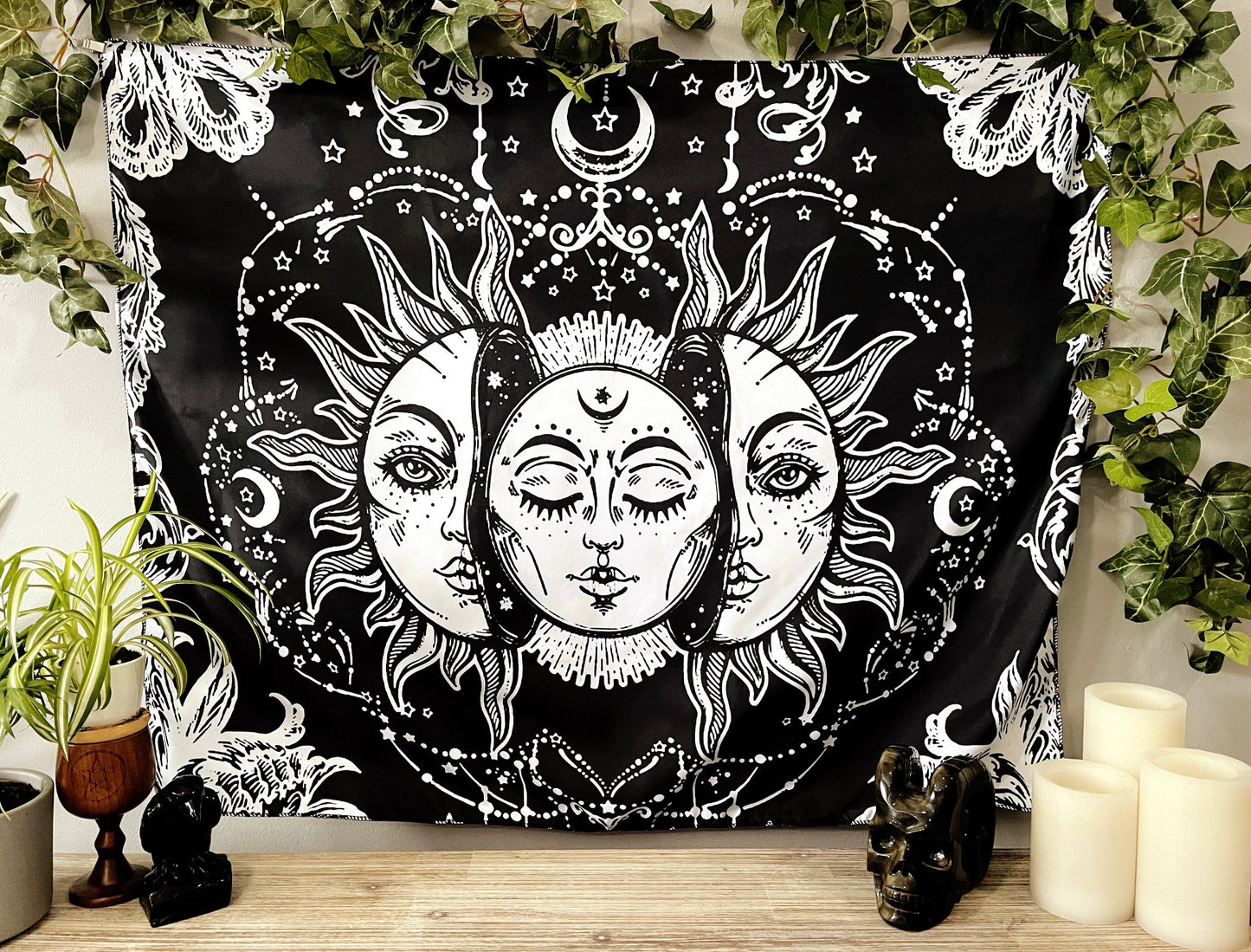 Pictured is a large wall tapestry with a black background and a large moon inside a sun printed in white on it. Moon & Sun Wall Tapestry