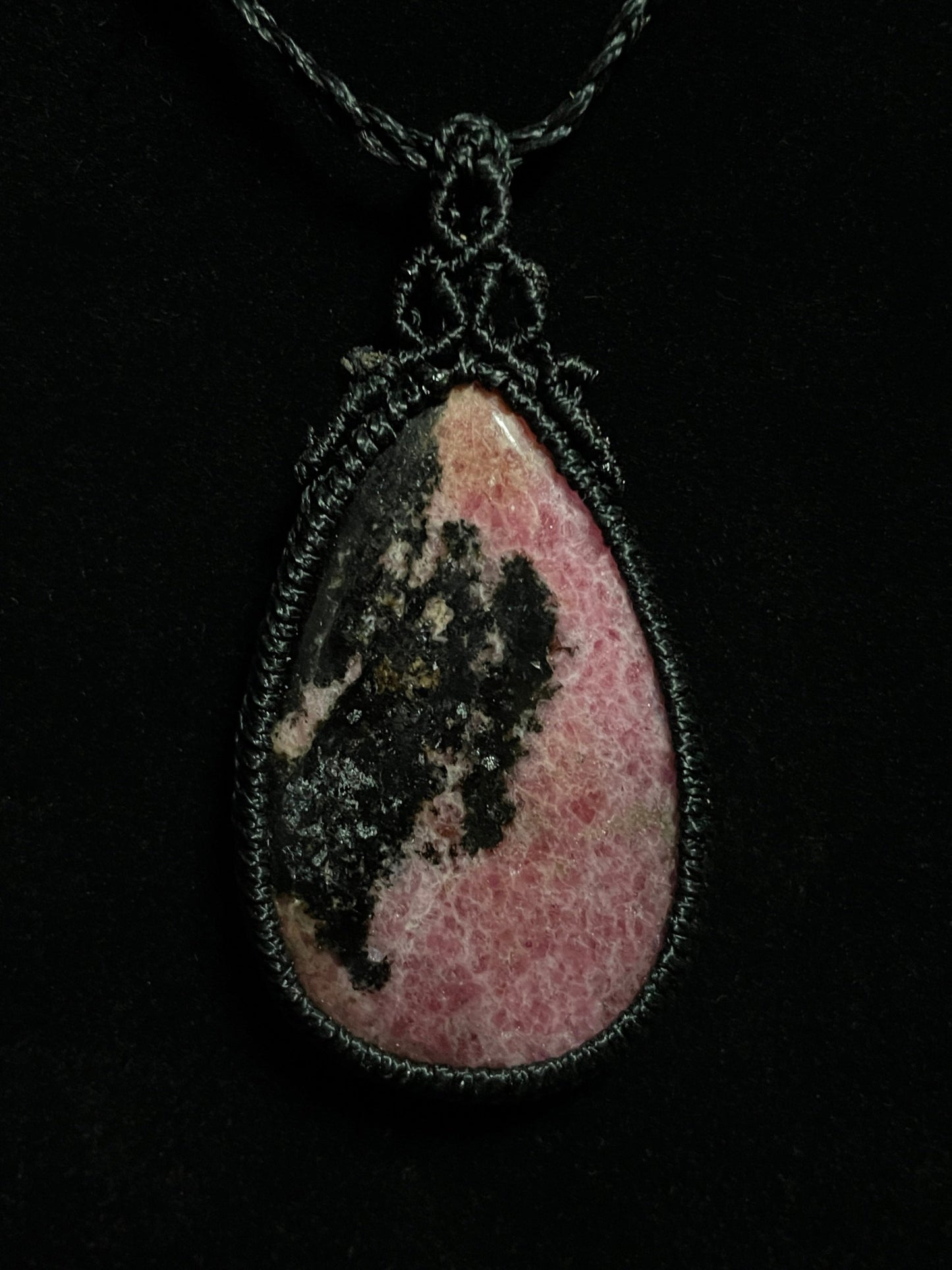 Pictured is a rhodonite cabochon wrapped in macrame thread. A gothic book and flowers are nearby. Rhodonite Macramé Necklace (Twisted Nightshade Jewellery) - The Wandering Fox Emporium, Your Crystal Store black