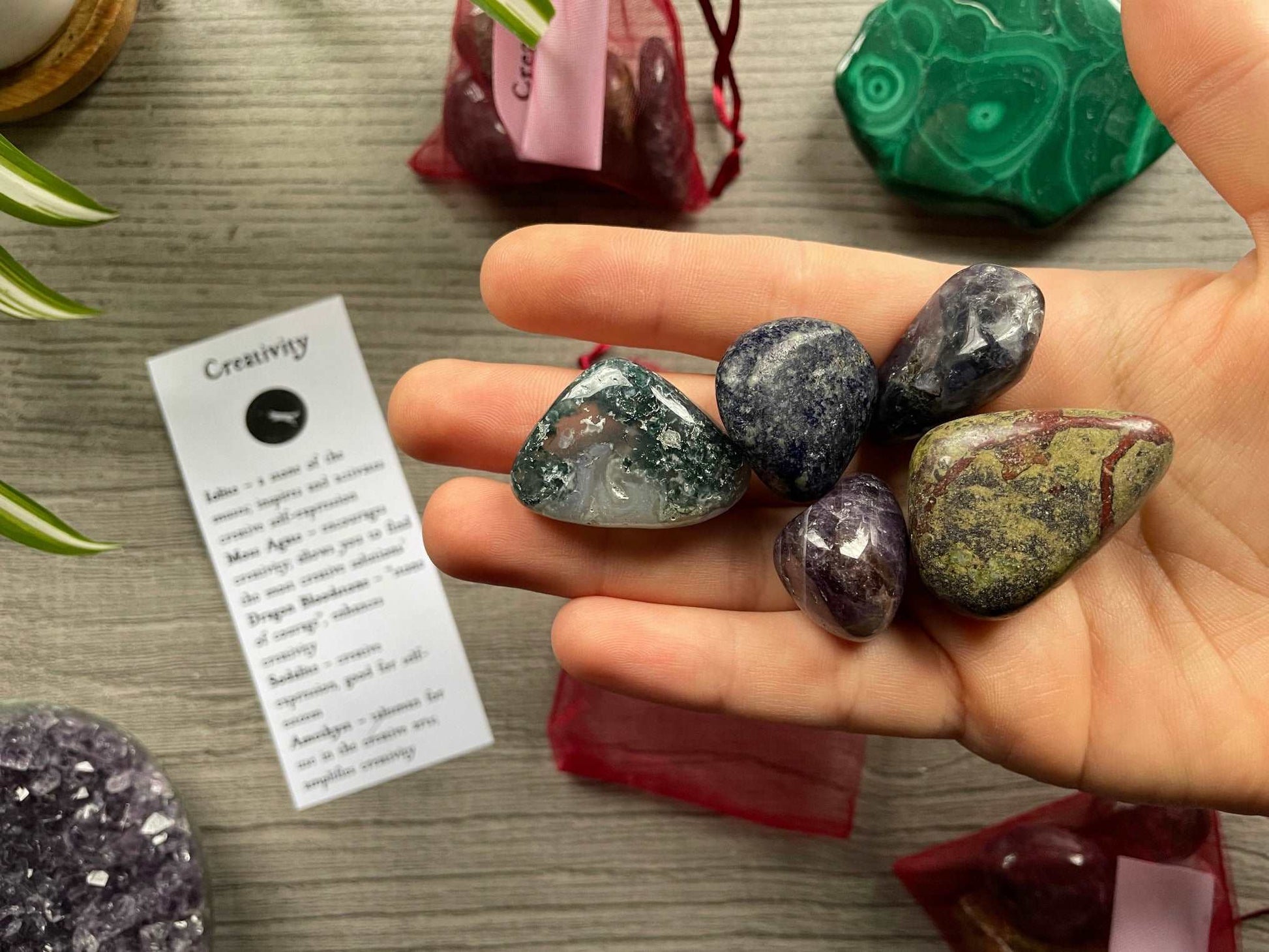 An image of a collection of tumbled stones in an organza bag. To the side is a piece of paper that describes what each tumbled stone's metaphysical properties are. CREATIVITY Tumbled Crystal Bag close up