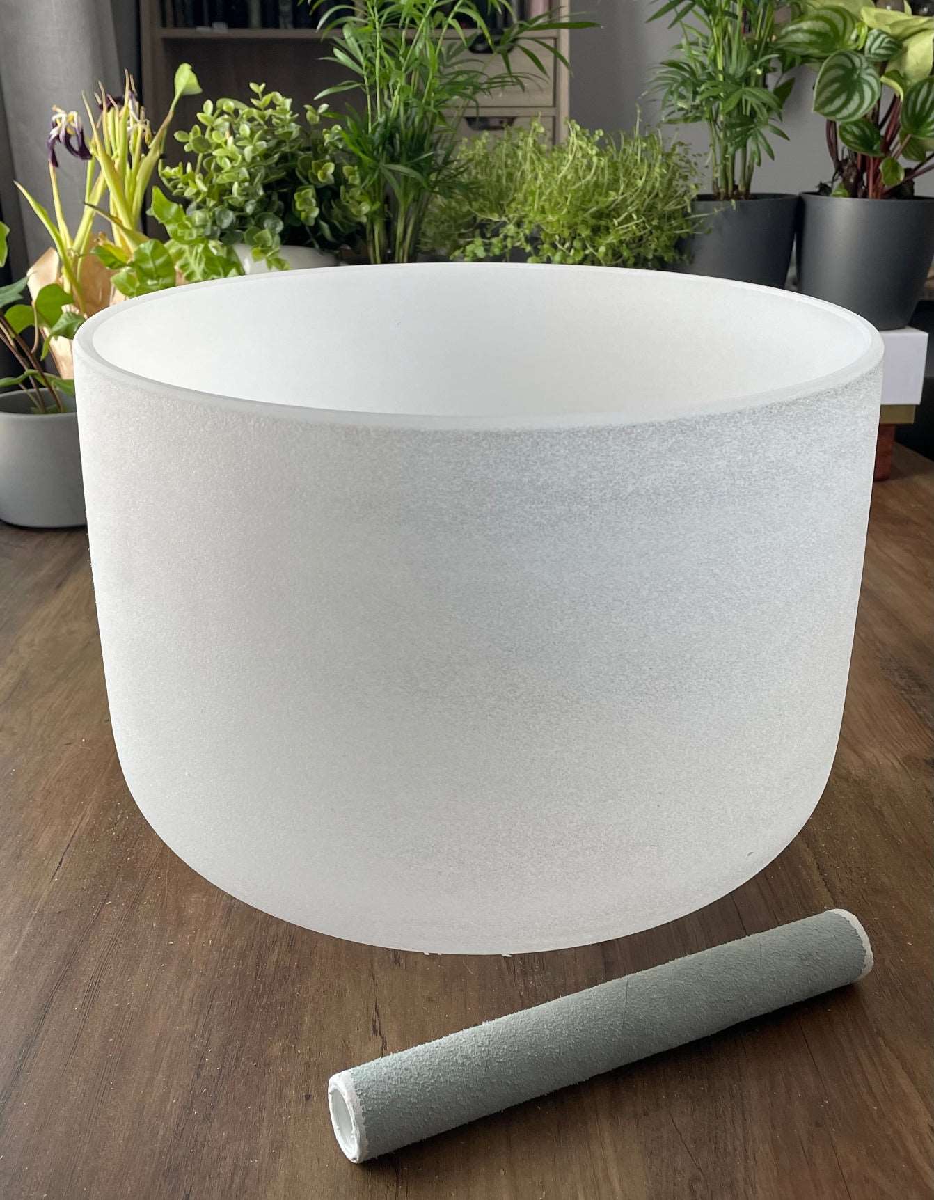  A photo of a quartz crystal singing bowl and a mallet on a wooden surface. The crystal singing bowl is made of clear quartz and has a smooth, round shape. 13" Crystal Singing Bowl (Frosted White) C4