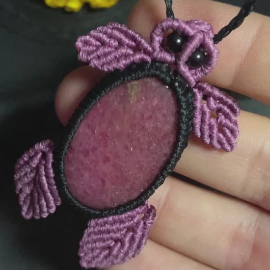 Pictured is a rhodonite cabochon wrapped in macrame thread. The rhodonite pendant is in the shape of a sea turtle. A gothic book and flowers are nearby. Rhodonite Sea Turtle Macramé Necklace (Twisted Nightshade Jewellery) Strawberry Quartz Pink Macramé Necklace (Twisted Nightshade Jewellery) - The Wandering Fox Emporium, Your Crystal Store video