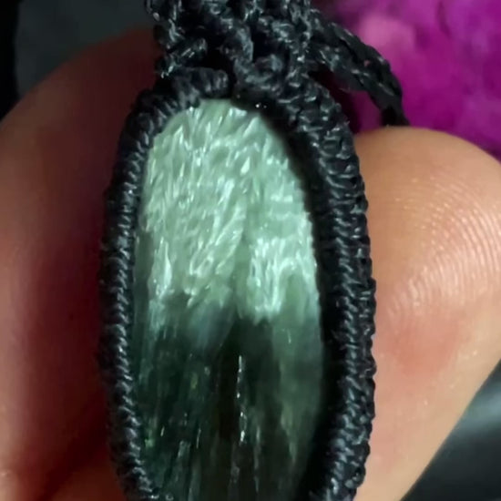 Pictured is a seraphinite cabochon wrapped in macrame thread. A gothic book and flowers are nearby. Seraphinite Macramé Necklace (Twisted Nightshade Jewellery) - The Wandering Fox Emporium, Your Crystal Store video