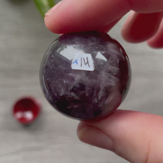 A polished sphere of amethyst is shown in the image. The crystal is a purple color and has a smooth, shiny surface. Amethyst Crystal Sphere 30mm (A) video
