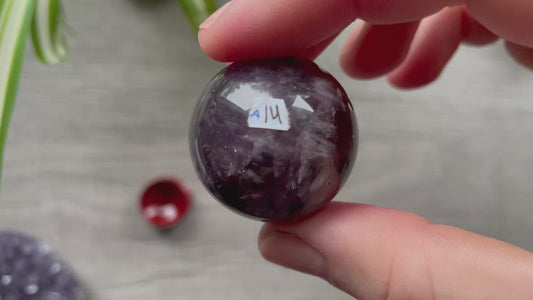 A polished sphere of amethyst is shown in the image. The crystal is a purple color and has a smooth, shiny surface. Amethyst Crystal Sphere 30mm (A) video