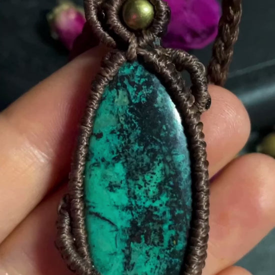 Pictured is a chrysocolla cabochon wrapped in macrame thread. A gothic book and flowers are nearby. Chrysocolla Macramé Necklace (Twisted Nightshade Jewellery) - The Wandering Fox Emporium, Your Crystal Store video