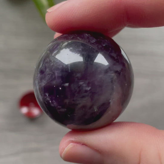 A polished sphere of amethyst is shown in the image. The crystal is a purple color and has a smooth, shiny surface. Amethyst Crystal Sphere 33mm video