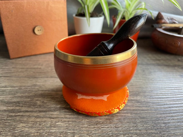 Pictured is a small metal singing bowl with a pillow and a wood gong mallet. Orange Singing Bowl (Sacral Chakra) 