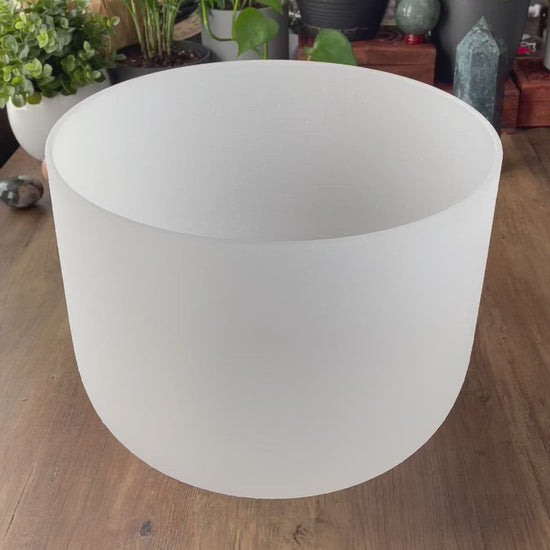  A photo of a quartz crystal singing bowl and a mallet on a wooden surface. The crystal singing bowl is made of clear quartz and has a smooth, round shape. video